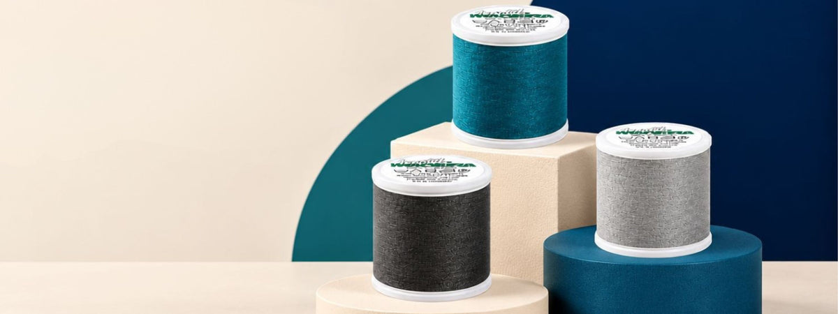 Three Madeira Aerofil thread spools in teal, charcoal, and light gray displayed on geometric pedestals against a modern navy, teal, and cream background.