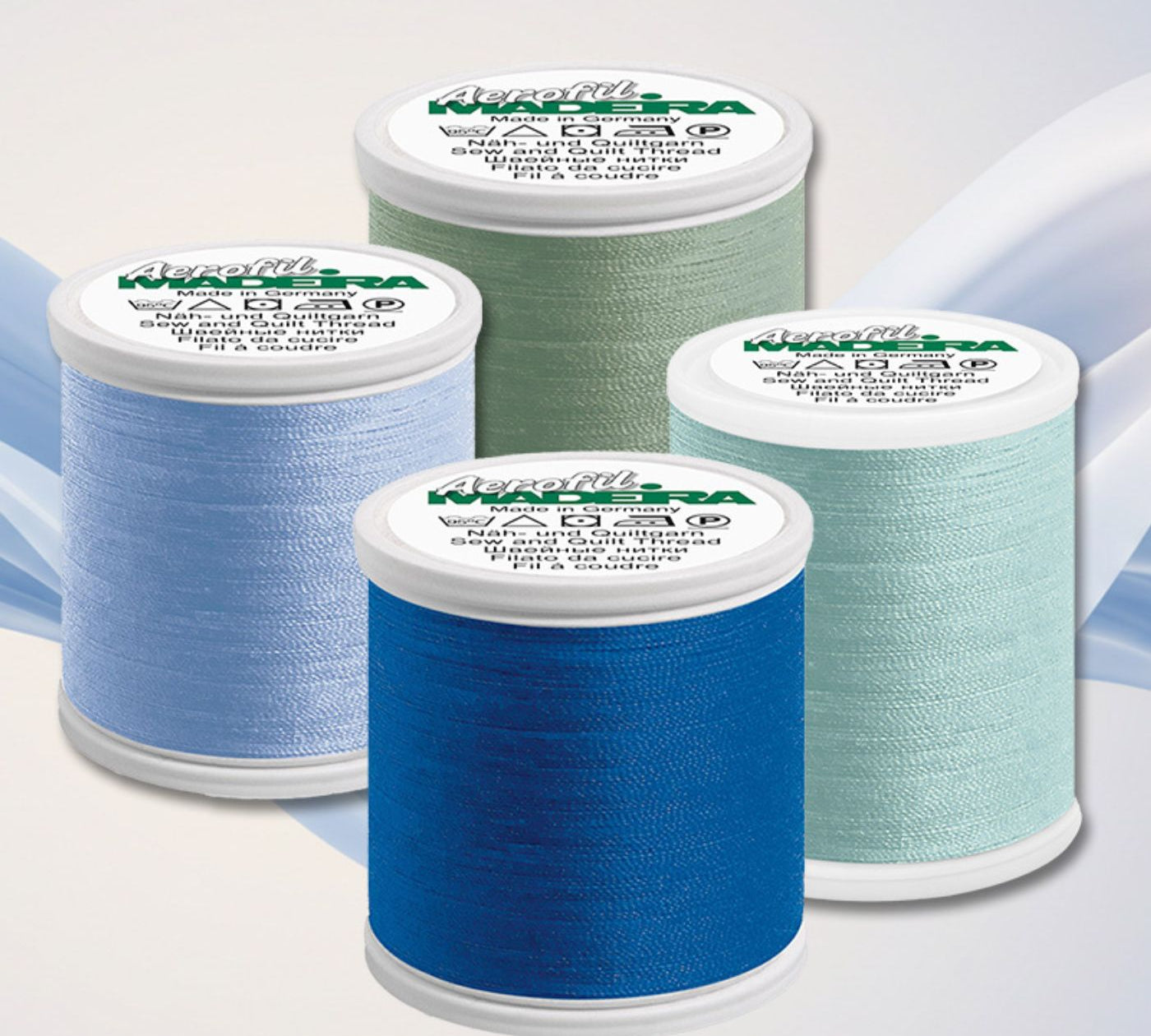 Four Madeira Aerofil sewing thread spools in blue, aqua, and green shades arranged on a soft abstract background.