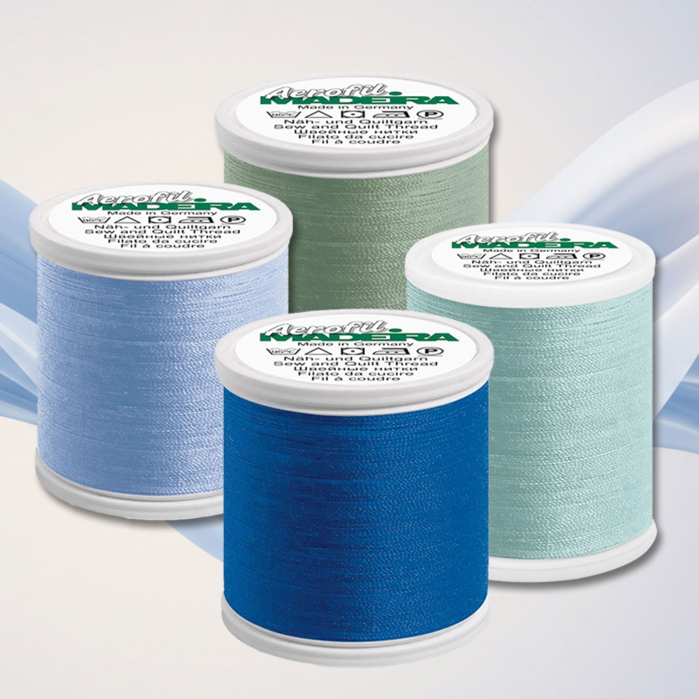 Four Madeira Aerofil sewing thread spools in blue, aqua, and green shades arranged on a soft abstract background.