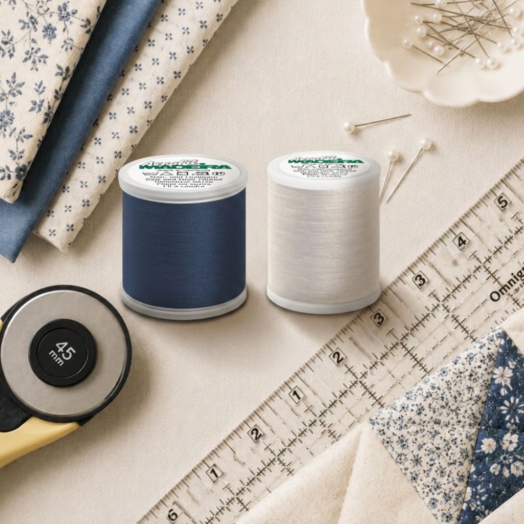 Madeira Aerofil all-purpose sewing thread spools in navy and white shown with quilting fabric, sewing pins, a ruler, and rotary cutter for sewing and quilting projects.