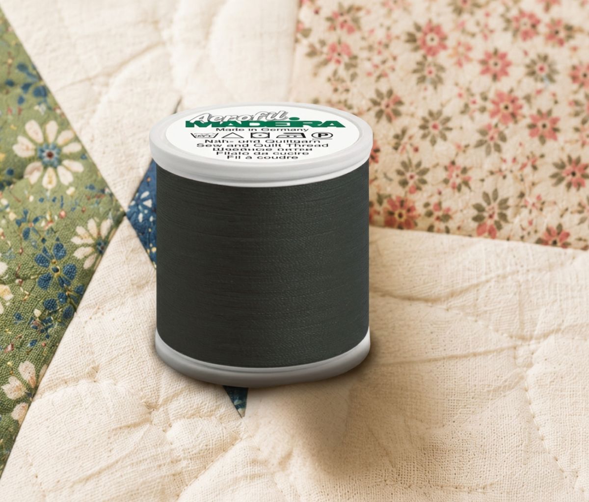 Madeira Aerofil all-purpose sewing thread in dark green shown on a quilted fabric background for sewing, quilting, and everyday stitching projects.