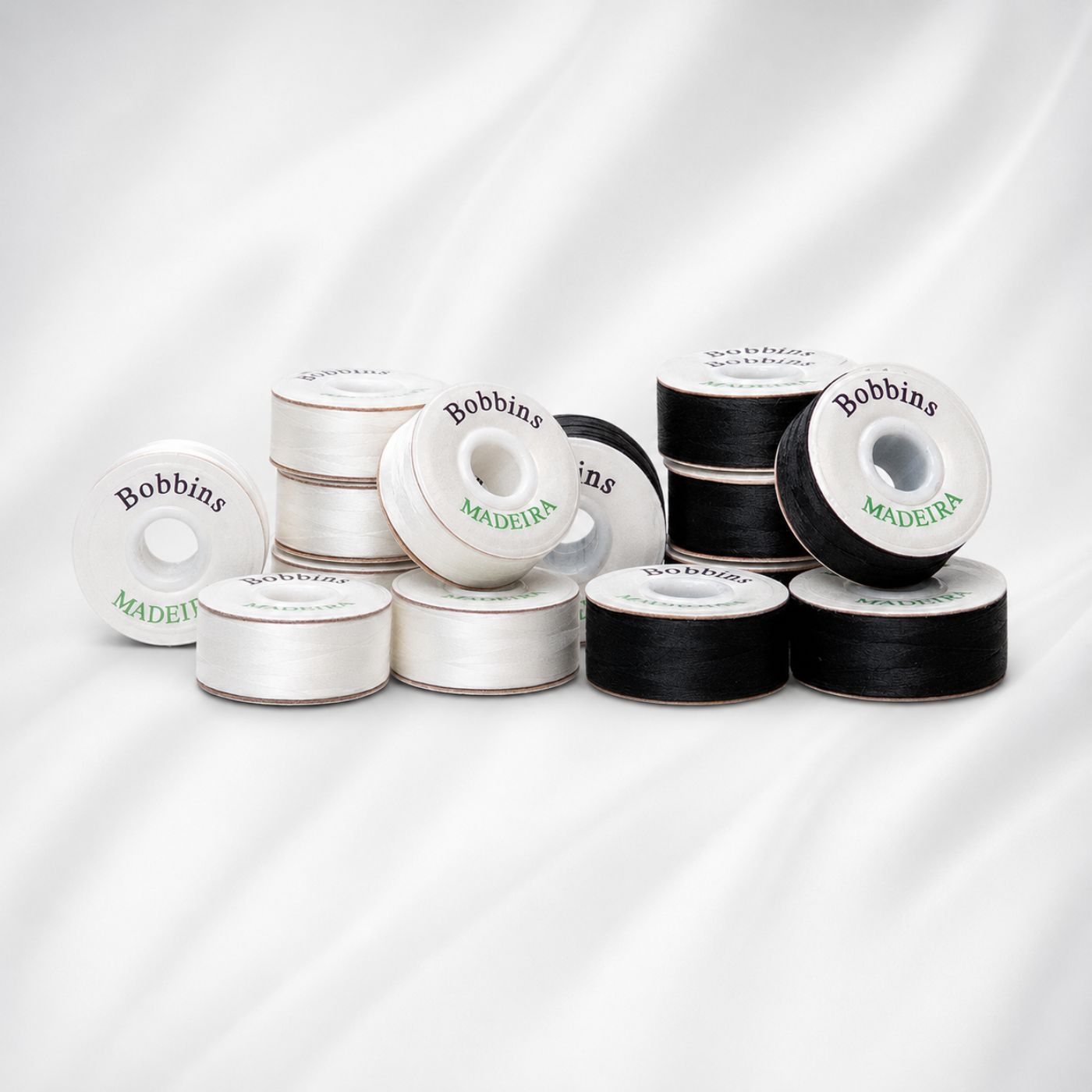 Madeira white and black bobbins arranged on a soft white background, showcasing prewound bobbin thread for sewing and quilting.