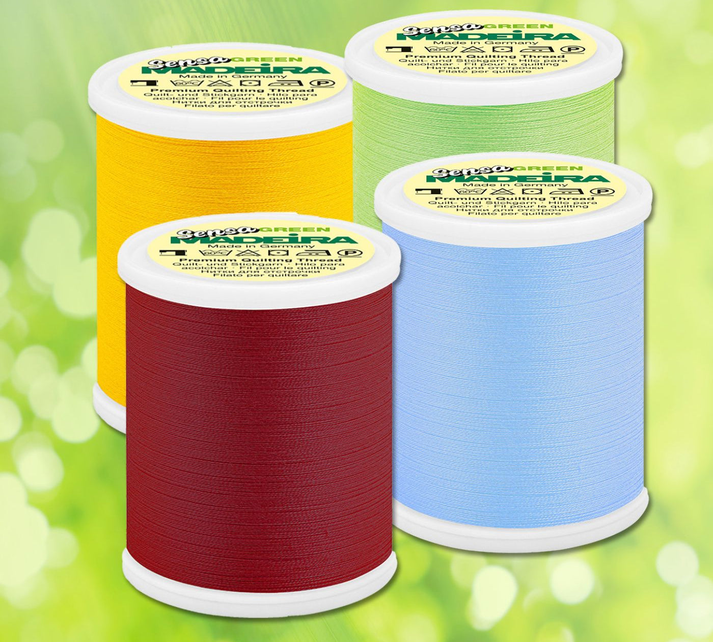 Four Madeira Sensa Green quilting thread spools in red, yellow, green, and light blue arranged on a soft green background.